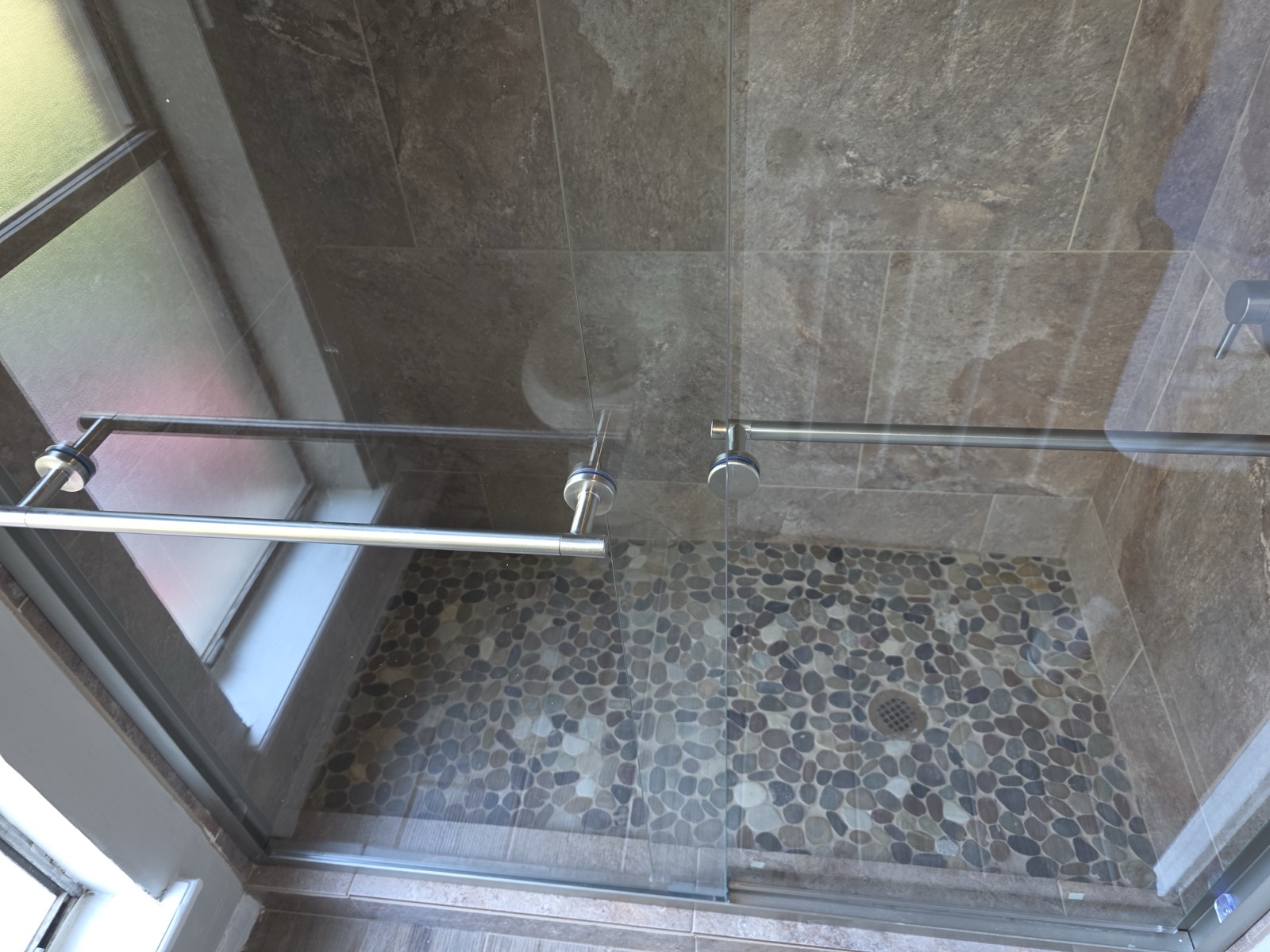 Wide slate shower with a pebble floor and a frameless glass panel