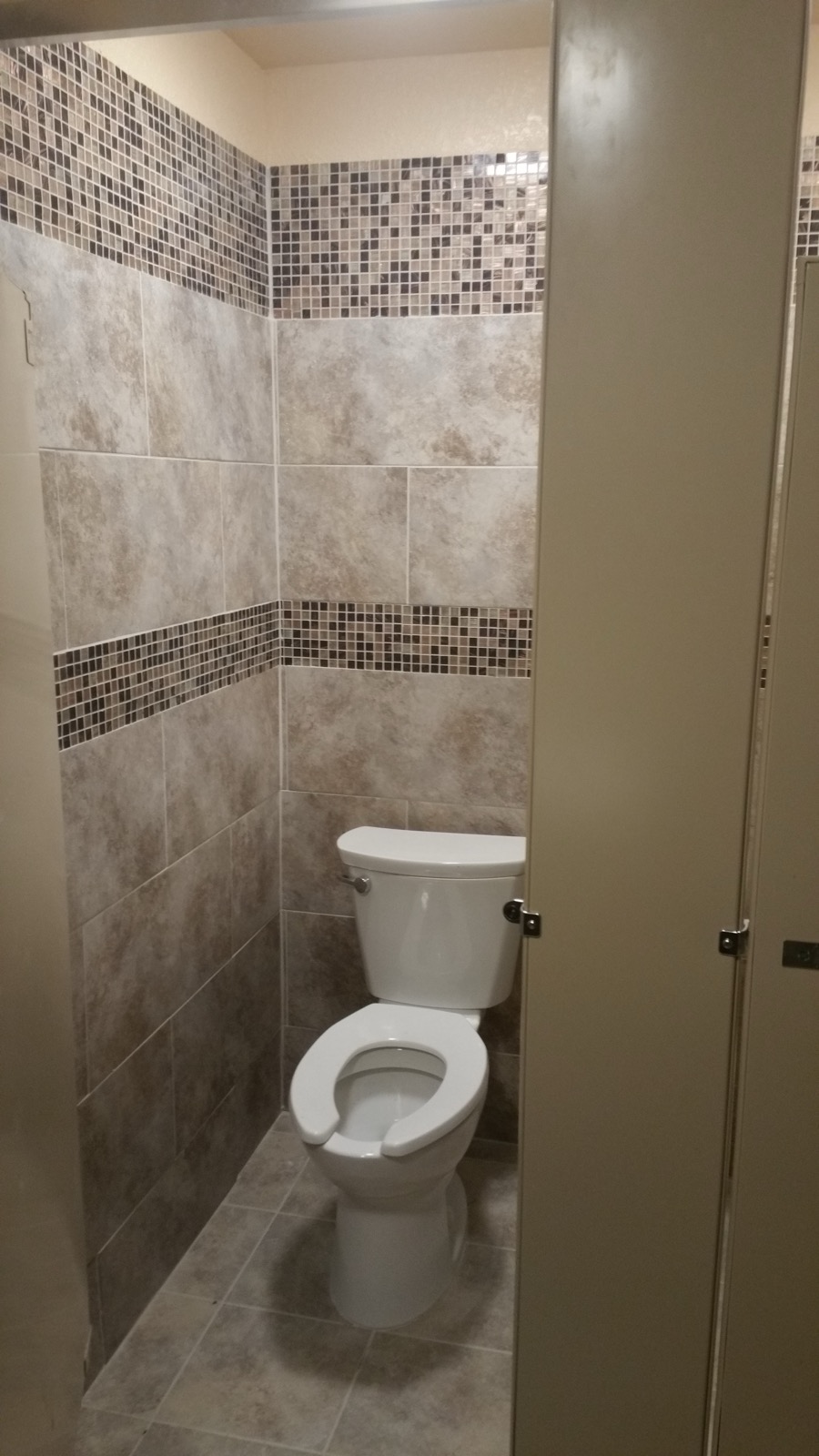 Commercial restroom with a tiled stall and a mosaic band