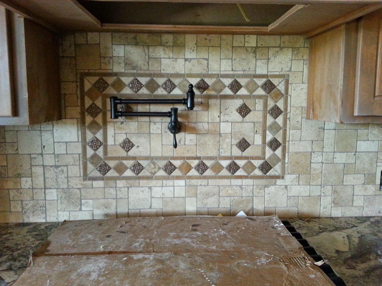 Travertine backsplash with a tile medallion and a pot filler